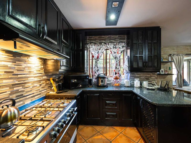 A well-appointed kitchen featuring dark cabinetry, granite countertops, a gas stove with extractor fan, and a decorative tiled backsplash.