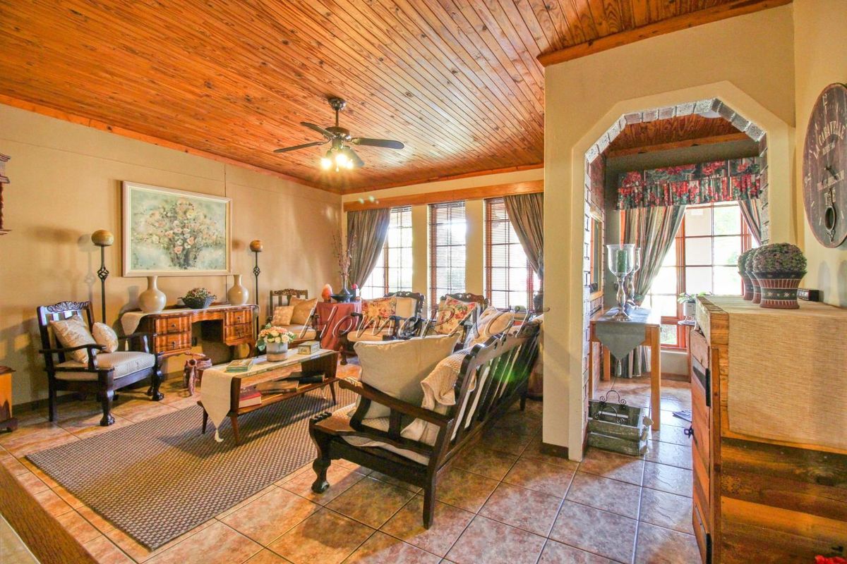 A cozy living room featuring a warm wood-paneled ceiling, tiled flooring, and an arched entryway leading to an adjacent space.