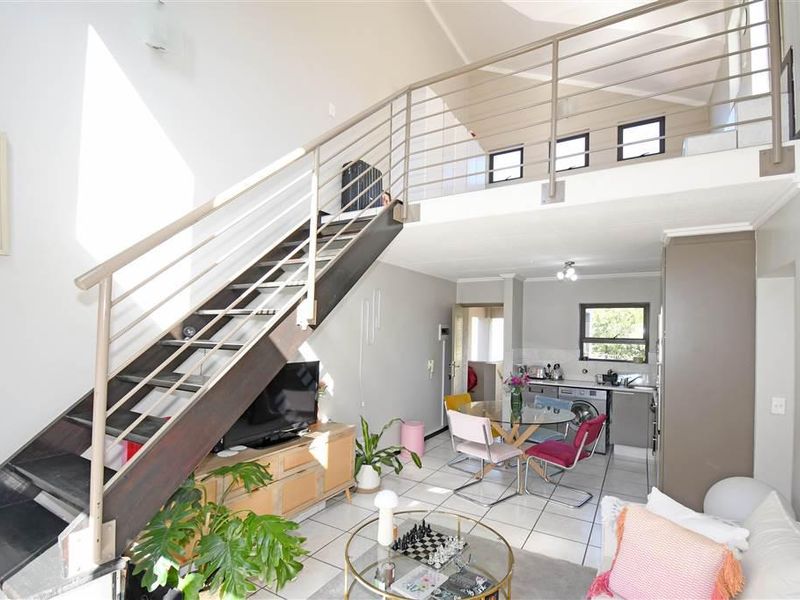 Open-plan living area featuring a mezzanine level, staircase with metal balustrade, tiled flooring, and a functional kitchen space with built-in cabinetry.
