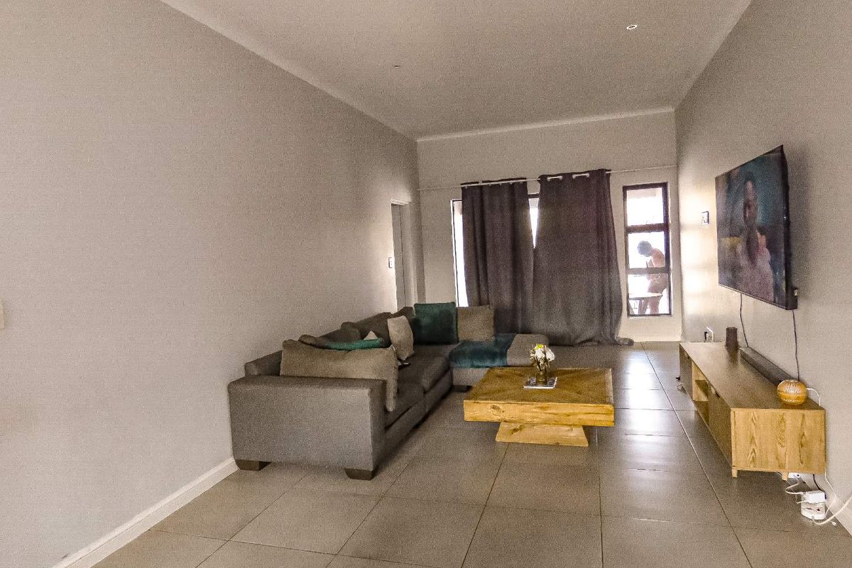 A spacious living room featuring neutral tiled flooring, recessed downlighting, and large windows with curtains, providing a comfortable and functional living area.