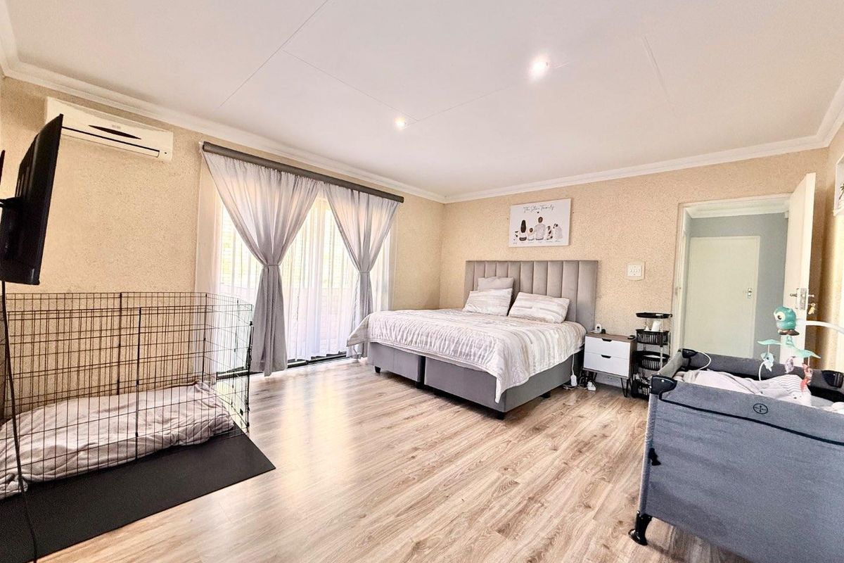 Spacious bedroom featuring light wood-look flooring, recessed ceiling lighting, and a wall-mounted air conditioning unit with access to a patio through sliding glass doors.