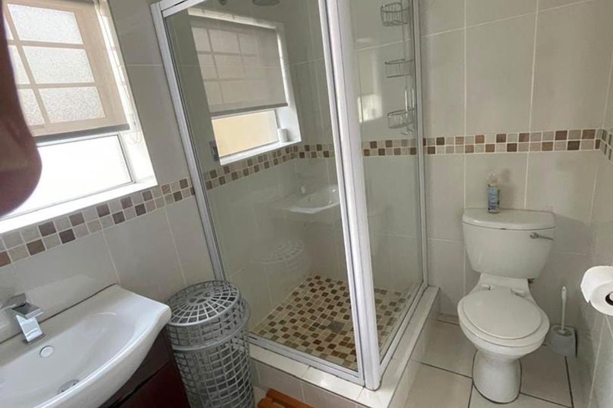 A functional bathroom featuring a glass-enclosed shower, a vanity basin with storage, and a standard toilet with tiled walls and flooring.
