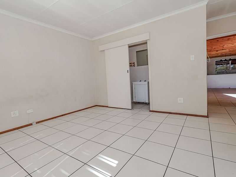 An empty bedroom featuring neutral tiled flooring, coving, and a sliding door leading to an en-suite area.