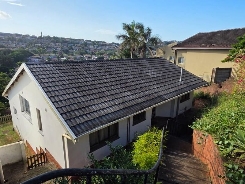Rear exterior view of the house featuring a tiled roof, concrete staircase with metal handrail, and surrounding garden area with brick retaining walls.