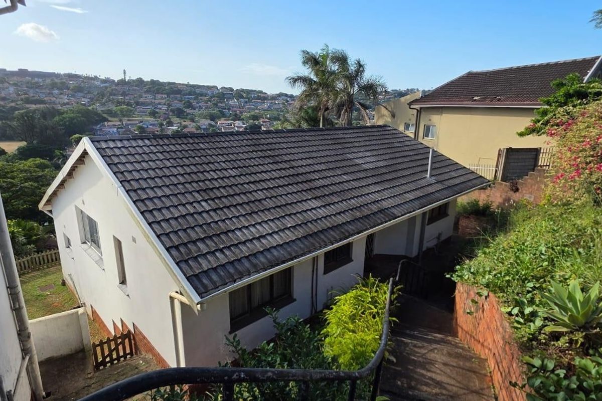 Rear exterior view of the house featuring a tiled roof, concrete staircase with metal handrail, and surrounding garden area with brick retaining walls.