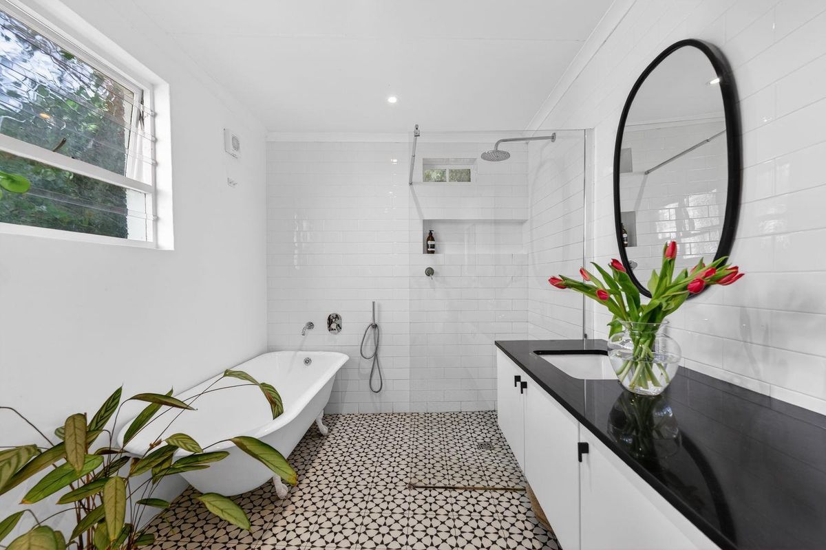 Modern bathroom featuring a freestanding bathtub, walk-in shower with niche, patterned floor tiles, and a sleek vanity with a stone countertop.