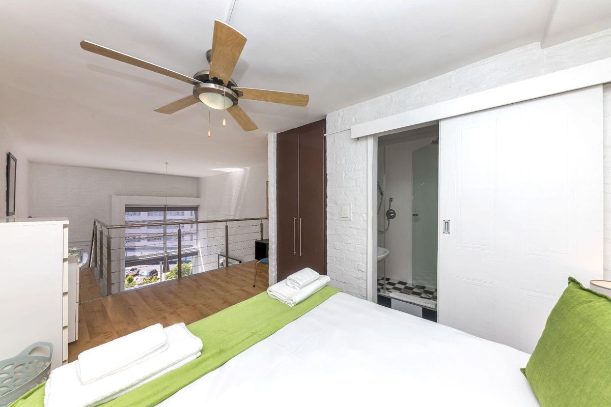 A loft-style bedroom featuring a mezzanine level, built-in wardrobe, ceiling fan, and an en-suite bathroom with a sliding door entrance.