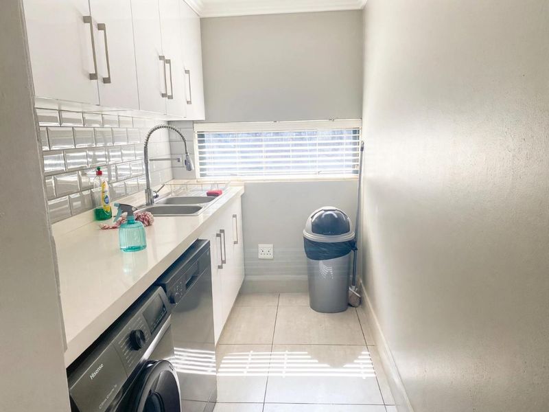 A clean and functional scullery featuring white cabinetry, subway tile backsplash, stone countertops, and a stainless steel sink with a modern gooseneck faucet.
