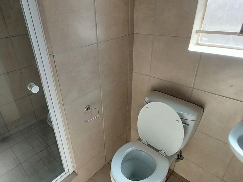 A functional bathroom featuring a shower enclosure, toilet, and wall-mounted basin with neutral wall and floor tiling.