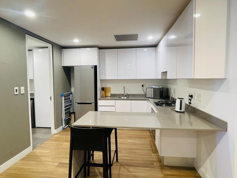 Modern kitchen featuring sleek white cabinetry, stone countertops, gas hob, and integrated stainless steel appliances with durable laminate flooring.
