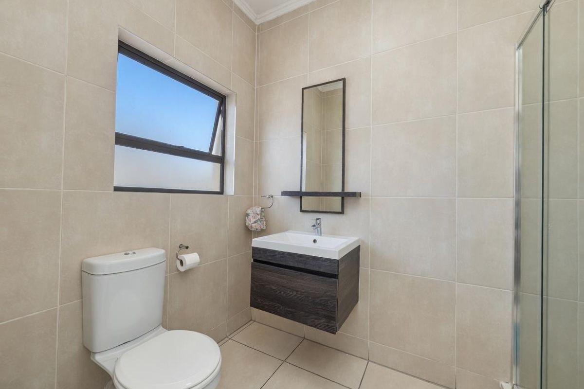 A modern bathroom featuring floor-to-ceiling neutral tiling, a wall-mounted vanity with basin, a toilet, and a glass-enclosed shower.
