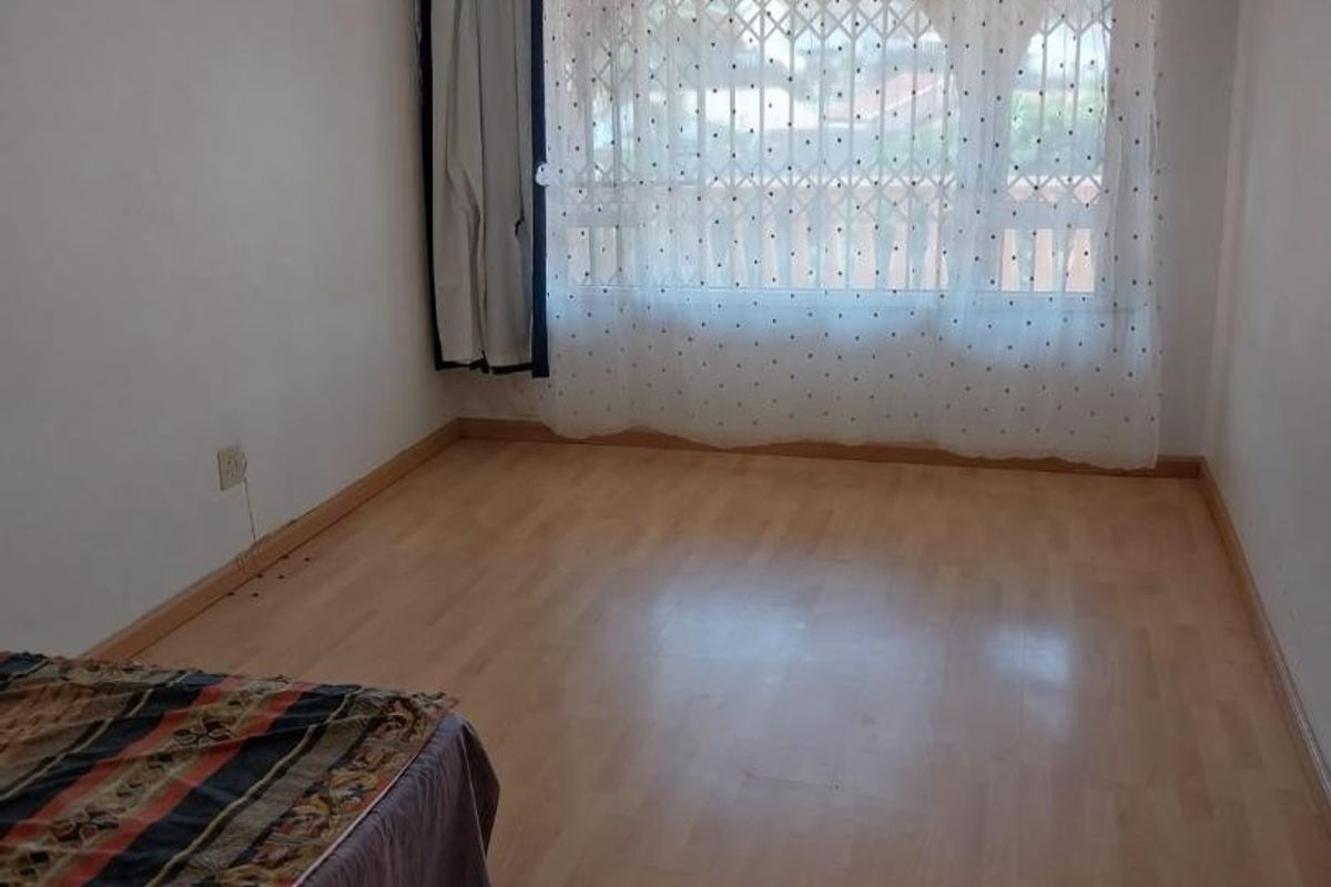 A simple, neutrally finished bedroom featuring laminate flooring and a window fitted with a security gate.