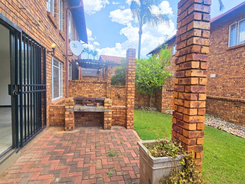 Rear exterior view of the townhouse featuring a paved patio area with a built-in brick braai and a small private garden space.