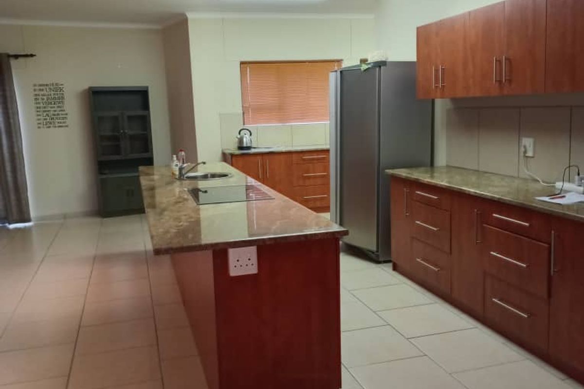 Spacious kitchen featuring a large central island with granite countertops, ample wooden cabinetry, and ceramic tile flooring throughout.