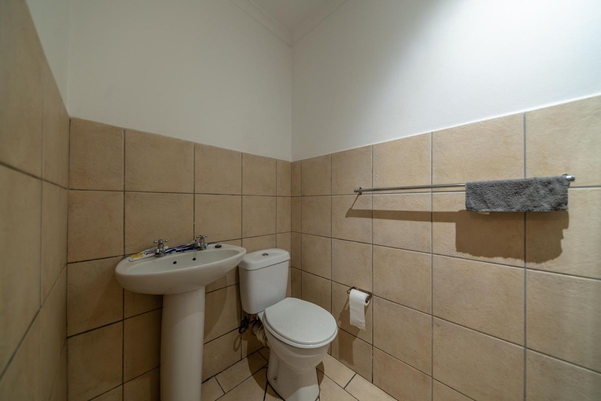 A functional guest bathroom featuring a pedestal basin, toilet, and neutral ceramic wall and floor tiling.