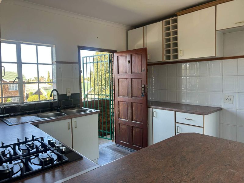 Functional kitchen featuring a gas hob, double sink, ample built-in cabinetry, and direct access to an outdoor area through a security gate.