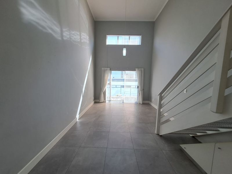 Spacious, double-volume living area featuring large format floor tiles, a modern staircase, and abundant natural light through sliding doors and a clerestory window.