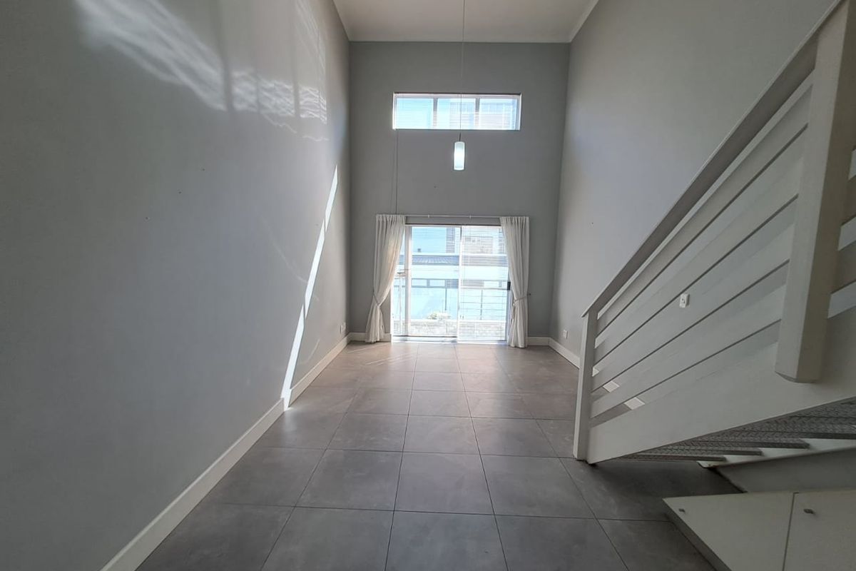 Spacious, double-volume living area featuring large format floor tiles, a modern staircase, and abundant natural light through sliding doors and a clerestory window.