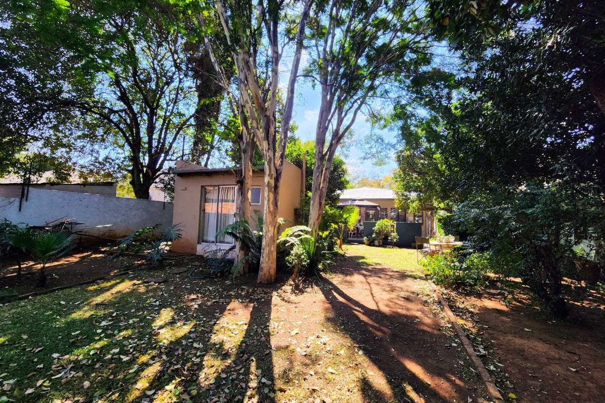A view of the rear garden featuring mature trees, a boundary wall, and a small outbuilding with a sliding glass door.