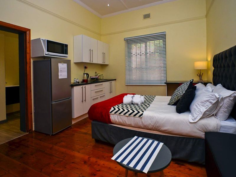 An open-plan studio apartment featuring a kitchenette with built-in cabinetry, timber flooring, and a bedroom area with neutral walls and classic cornicing.