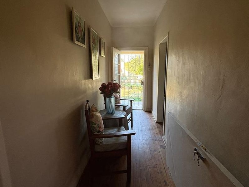 A narrow hallway featuring timber flooring and access to an exterior security gate, showing signs of wear on the walls and floors.