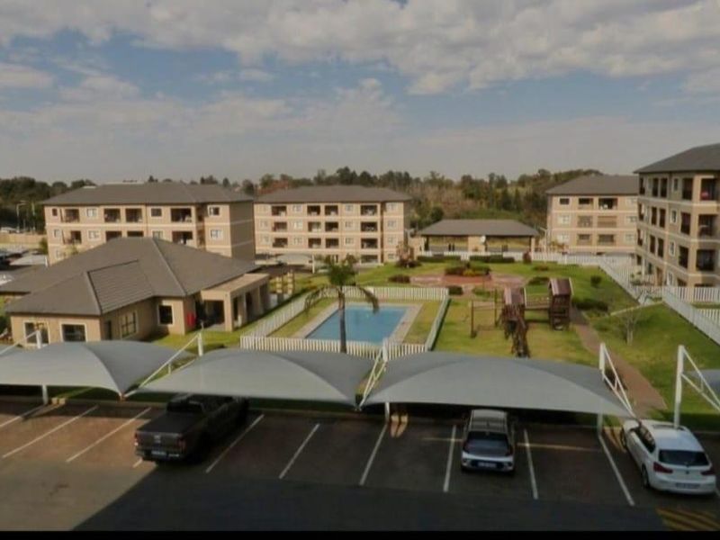 Aerial view of the apartment complex featuring a central swimming pool, landscaped garden, and covered parking bays for residents.