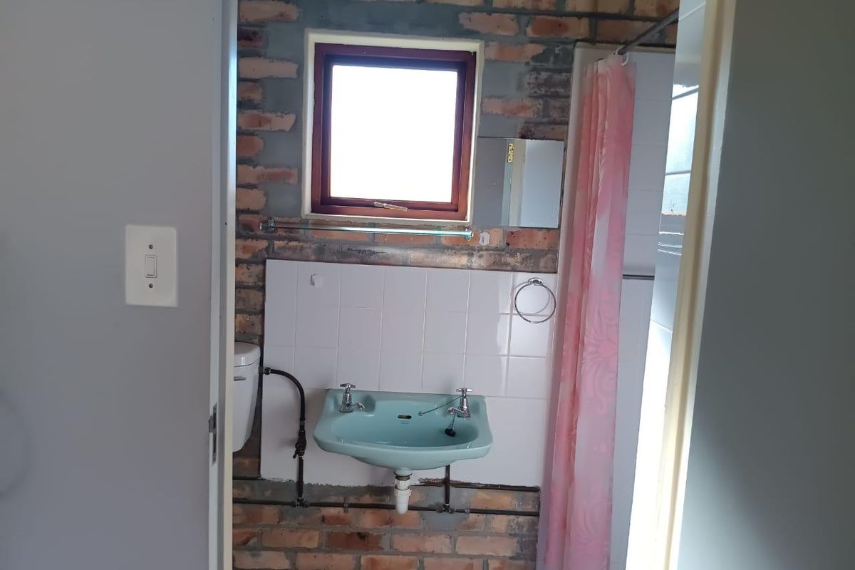 A compact bathroom featuring exposed brick walls, a wall-mounted basin, and a shower area with a curtain.