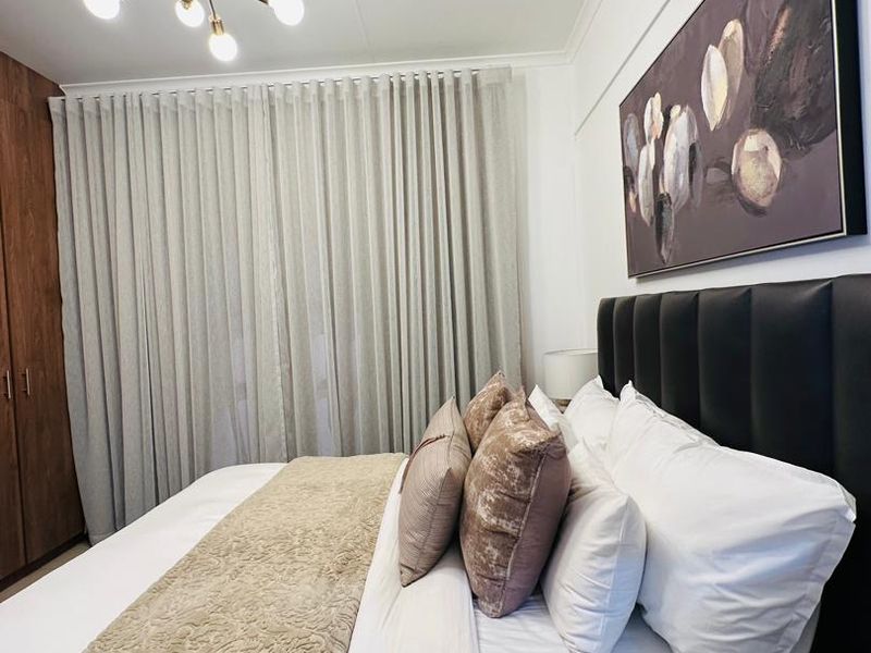 A well-maintained bedroom featuring built-in cupboards, a split-system air conditioner, and a contemporary chandelier, offering a comfortable and functional living space.