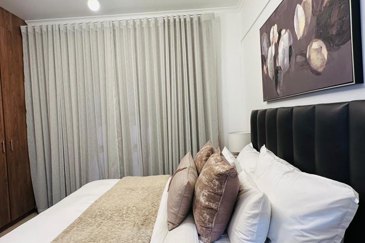 A well-maintained bedroom featuring built-in cupboards, a split-system air conditioner, and a contemporary chandelier, offering a comfortable and functional living space.