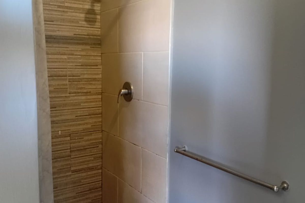 A functional bathroom shower area featuring a pebble floor, tiled walls, and a modern shower mixer fixture.