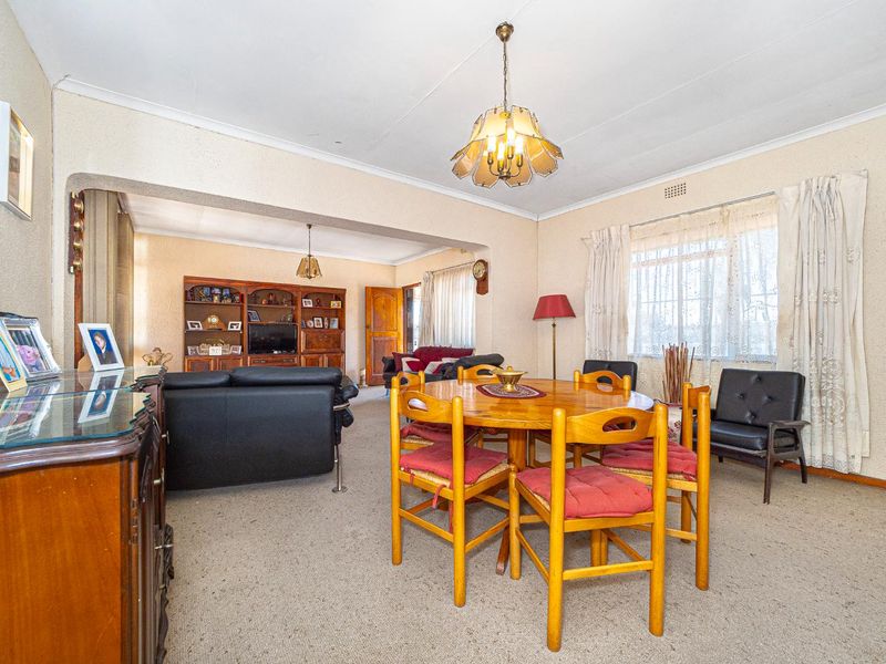 An open-plan living and dining area featuring carpeted flooring, coved ceilings, and built-in cabinetry, offering a functional layout with potential for modernization.