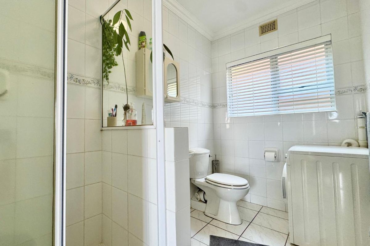 A functional bathroom featuring a glass-enclosed shower, toilet, and tiled flooring, with integrated space for laundry appliances.