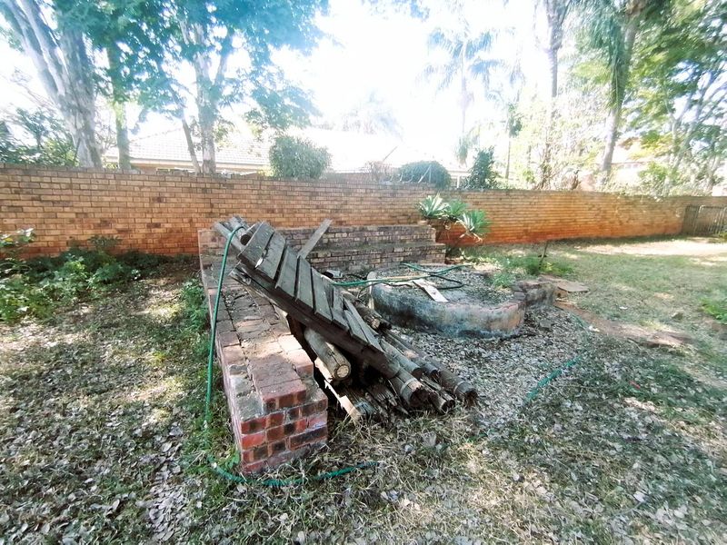 A rear garden area featuring a brick boundary wall, a low brick retaining wall, and a circular brick fire pit, currently requiring significant landscaping maintenance.