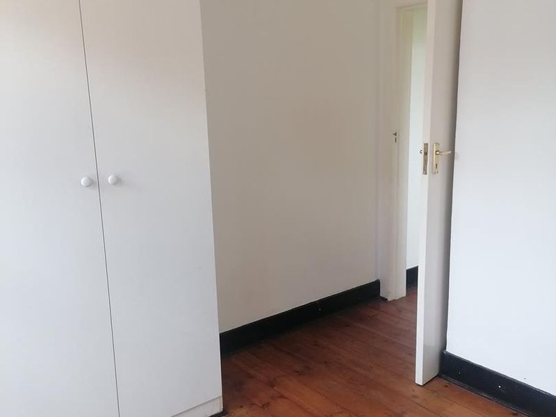 A vacant bedroom featuring polished timber flooring, white walls, and a built-in wardrobe with a doorway leading to an adjacent space.