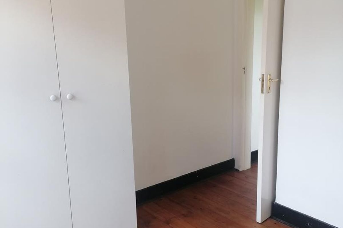 A vacant bedroom featuring polished timber flooring, white walls, and a built-in wardrobe with a doorway leading to an adjacent space.