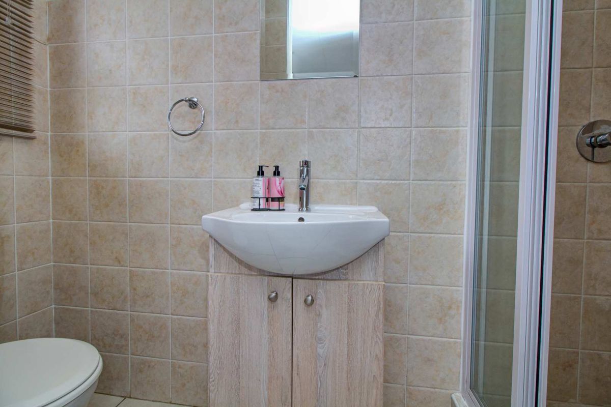 A functional bathroom featuring a vanity cabinet with a basin, a shower enclosure, and neutral wall tiling.