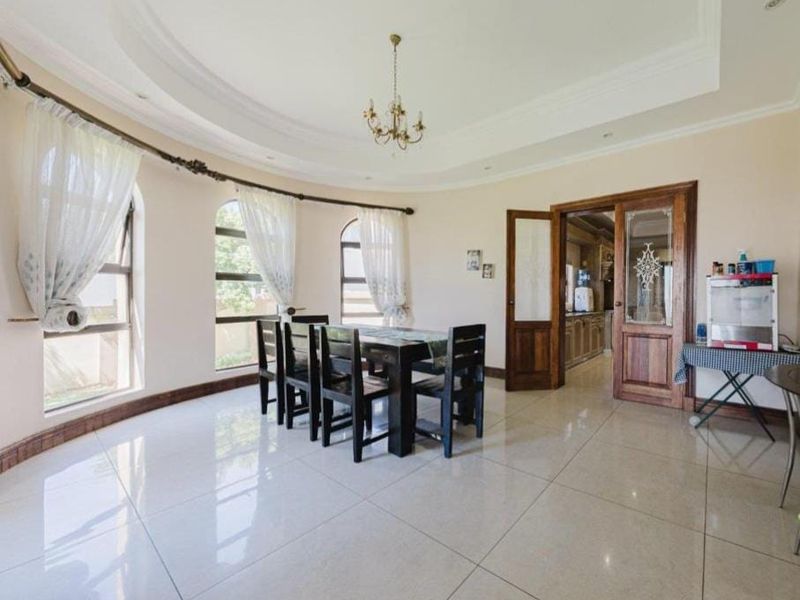 Spacious dining room featuring elegant arched windows, a recessed ceiling detail, and polished tile flooring, with direct access to the kitchen area.