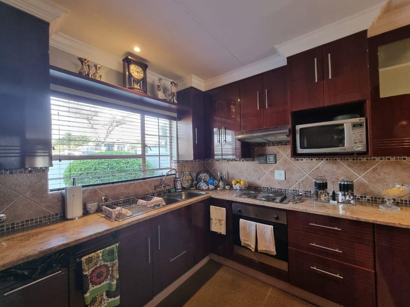 A well-maintained kitchen featuring dark wood cabinetry, granite countertops, built-in appliances, and a tiled backsplash with a window overlooking the exterior.