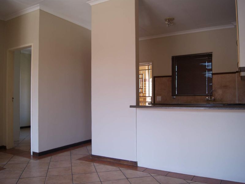 An open-plan living area featuring tiled flooring and a functional kitchen with a breakfast bar, neutral walls, and natural light.