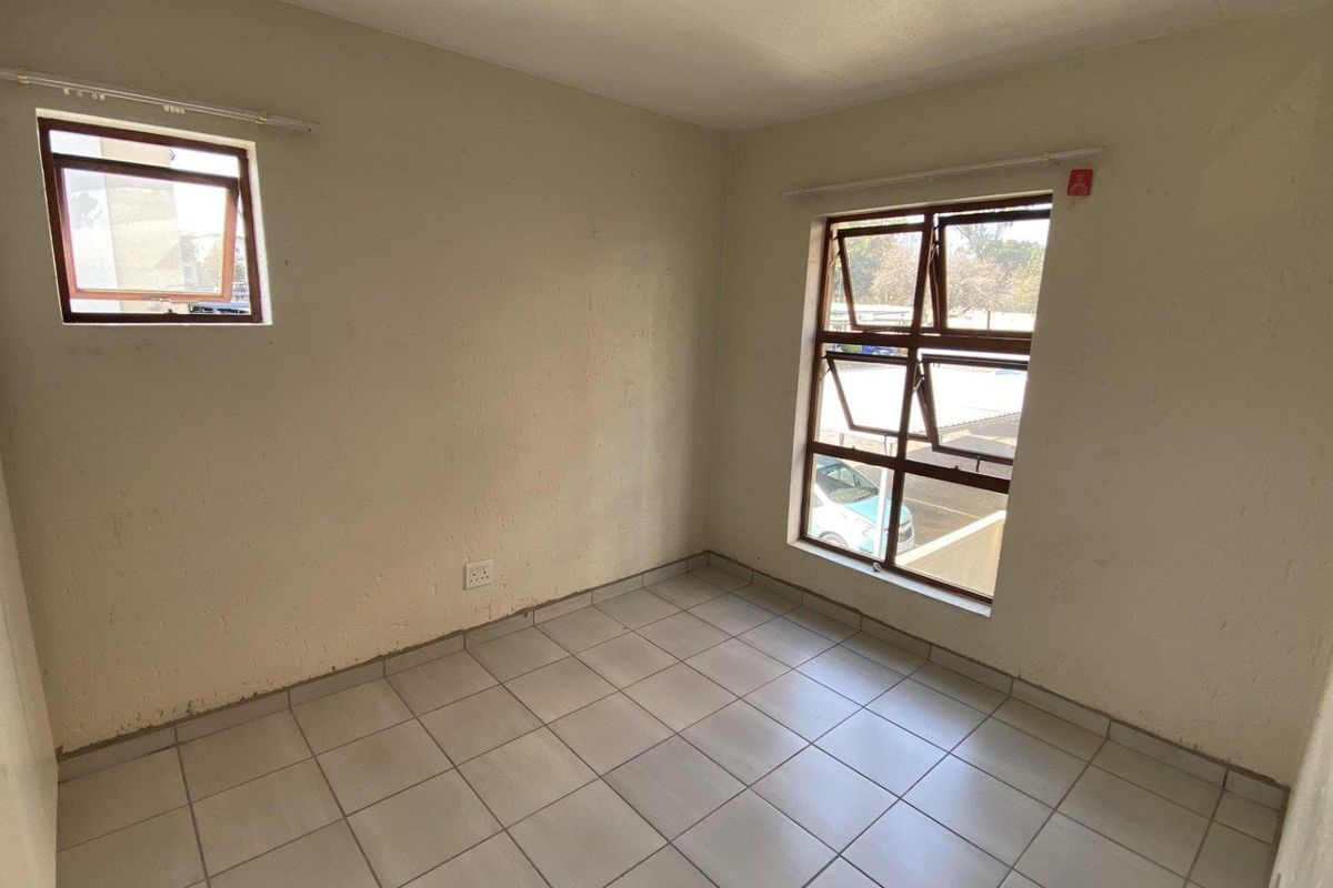 A vacant bedroom featuring neutral tiled flooring, built-in storage, and aluminium-framed windows providing natural light.