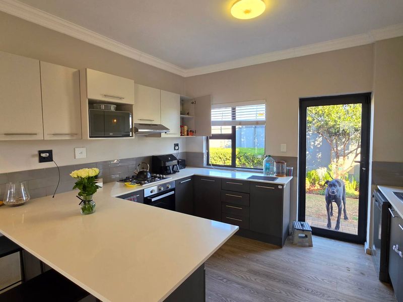 Modern kitchen featuring two-tone cabinetry, quartz countertops, integrated appliances, and direct access to the rear garden through a glass-panelled door.