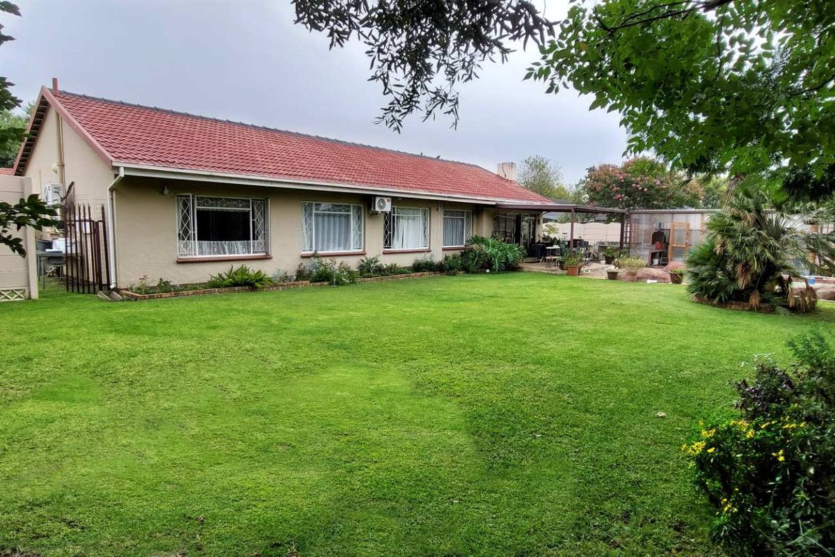 A spacious rear garden featuring a well-maintained lawn, perimeter wall, and a view of the rear facade of the house with a tiled roof.