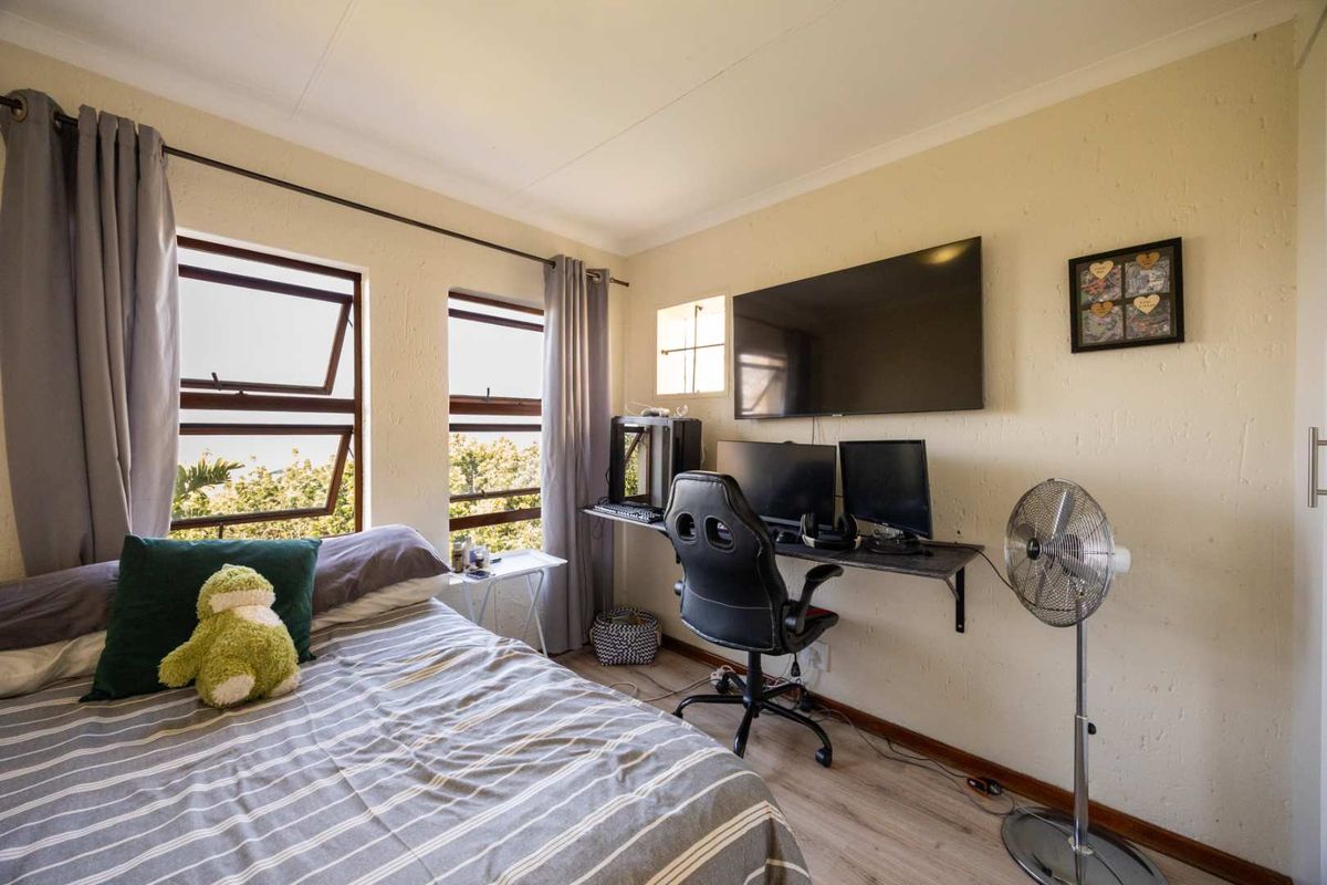 A functional bedroom featuring laminate flooring, dual casement windows, and neutral wall finishes, currently utilized as a combined sleeping and workspace area.
