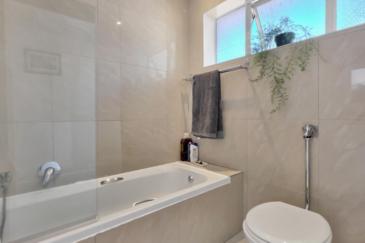 Modern bathroom featuring a built-in bathtub with a glass screen, wall-mounted toilet, and neutral floor-to-ceiling wall tiles.