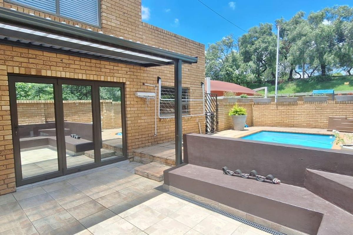 Rear exterior view featuring a paved patio area, built-in bench seating, and a private swimming pool enclosed by brick boundary walls.