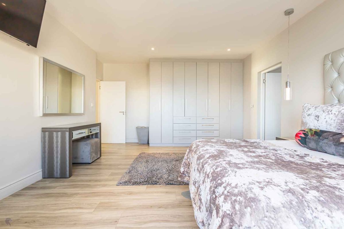 Spacious bedroom featuring light wood-look flooring, recessed ceiling lighting, and extensive built-in floor-to-ceiling cabinetry with integrated drawers.