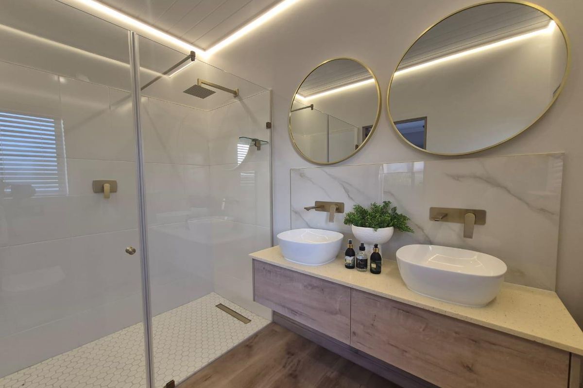 Modern bathroom featuring a walk-in glass shower, dual vessel sinks on a floating vanity, and elegant gold-toned fixtures with integrated LED lighting.