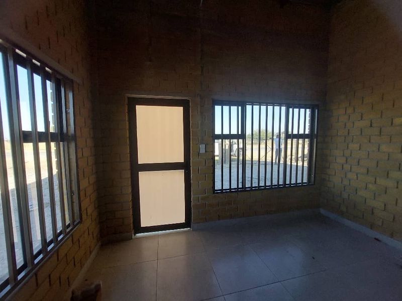 An unfinished open-plan industrial space featuring exposed brick walls, tiled flooring, and secure aluminium-framed windows and door.