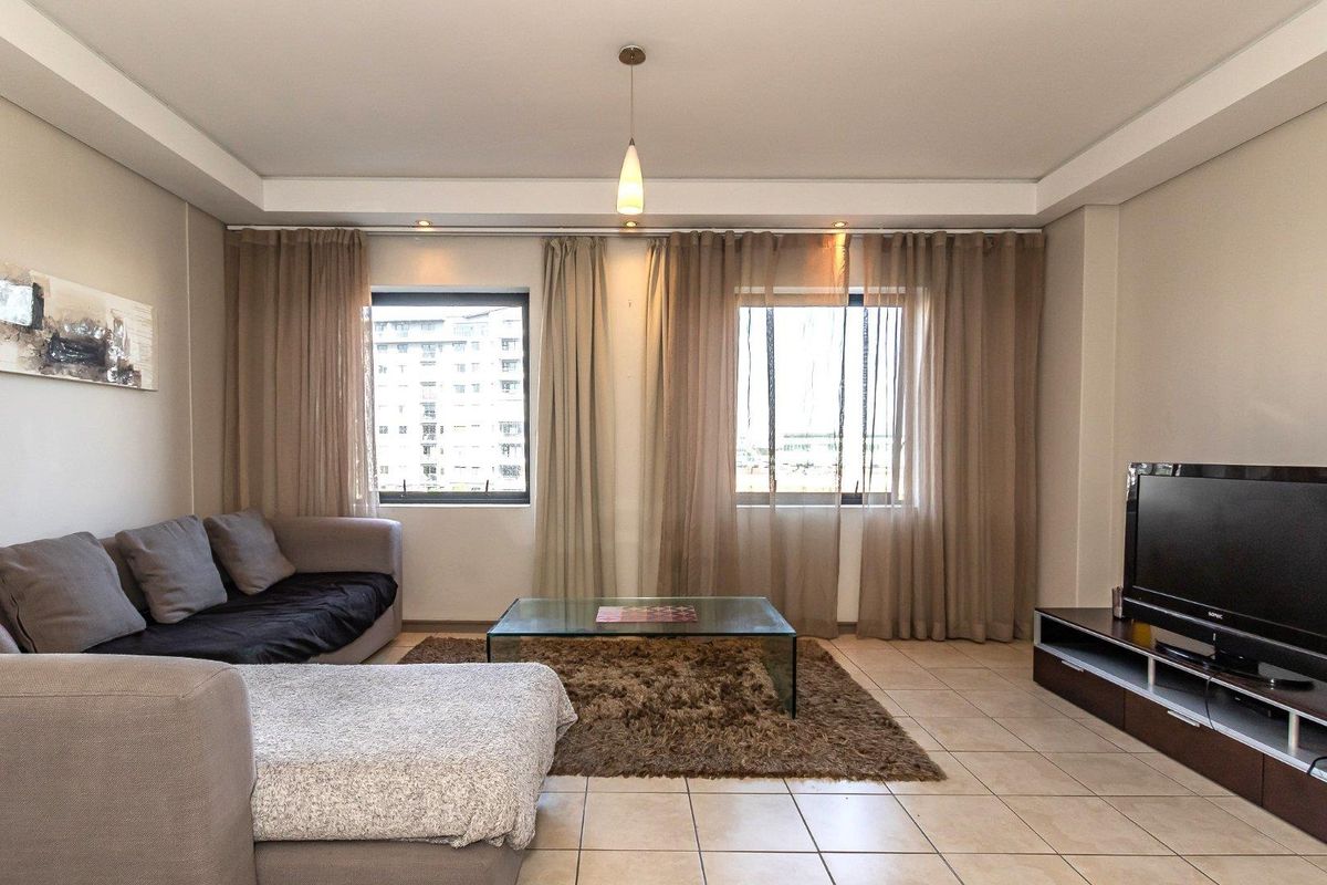 A comfortable living room featuring tiled flooring, recessed ceiling detailing, and large windows that allow for natural light.