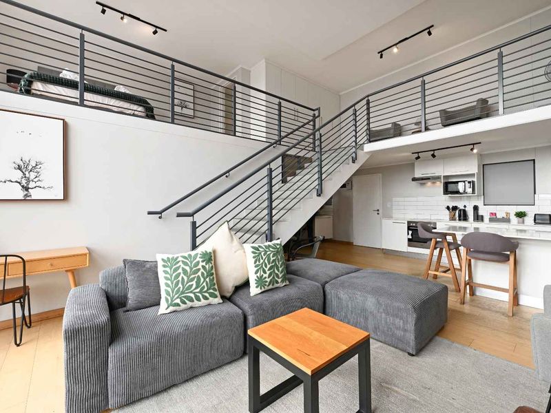Modern open-plan penthouse living area featuring a mezzanine level, sleek kitchen cabinetry, integrated appliances, and contemporary staircase design with high-quality finishes.